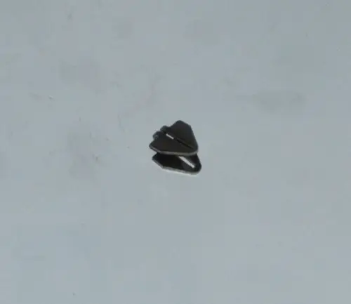 Schwarze Abstandsklammer von Daikin, platziert auf einem glatten Untergrund. Die Klammer hat eine symmetrische Form mit zwei überlappenden Teilen.